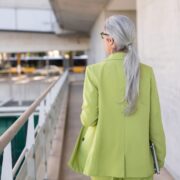 Grey haired woman in office wearing green coat.