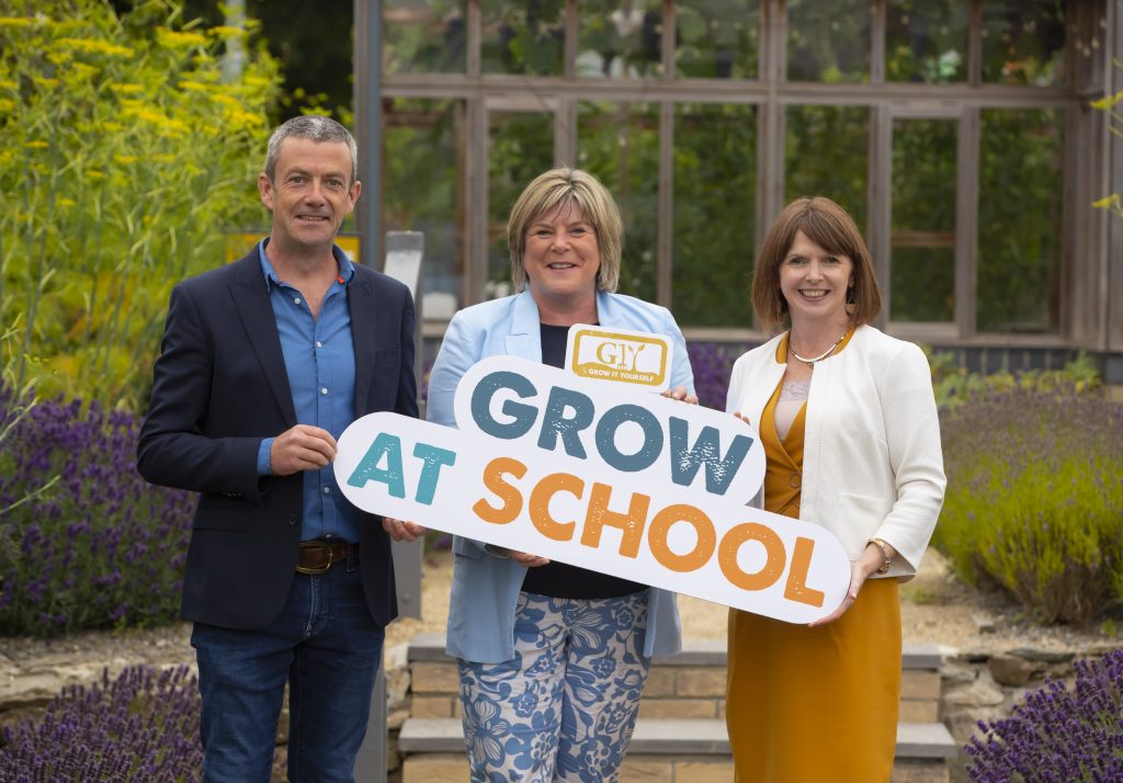 Two women and a man holding a sign saying Grow at School.