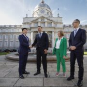 3 men in dark business suits and 1 woman in a green business suit at Government buildings in Dublin.