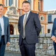 Three men in business suits outside a red brick building.