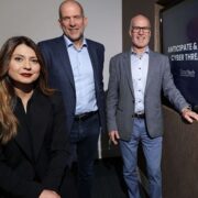 Woman in black coat beside two men in sports jackets.