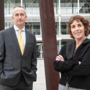 Man and woman standing in front of buildings.