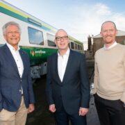 Three men standing between trains.
