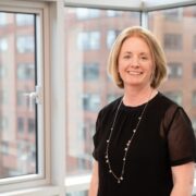 Woman in black dress beside a window.