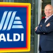 Man in suit beside an ALDI sign.