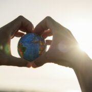 Hand making a love heart gesture while holding a globe.