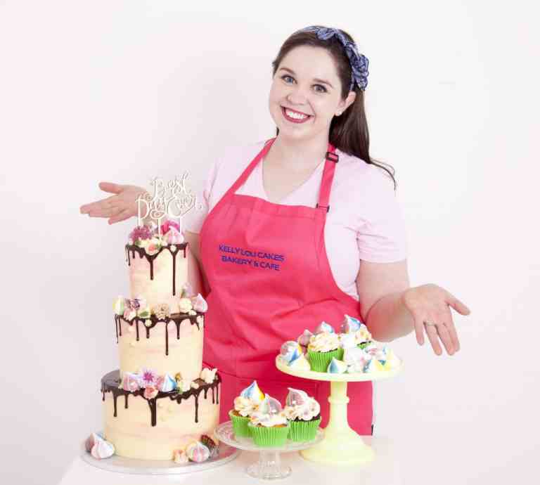 Woman in pink apron behind cakes.