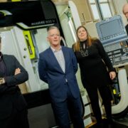 Three men and a woman in front of an industrial milling machine.