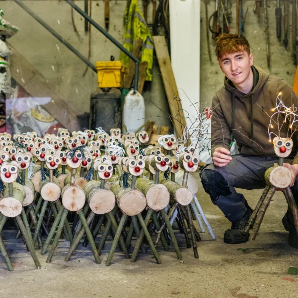 Young man beside ranks of wooden reindeer.