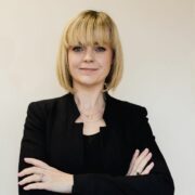 Fair haired woman wearing black business suit.