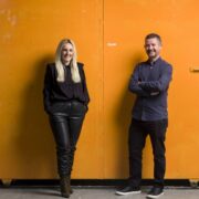 Man and woman in front of an orange wall.