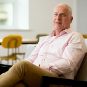 Man in salmon shirt sitting in chair.