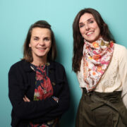 Two women in front of green background.