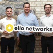 Three men holding a sign saying Elio Networks.