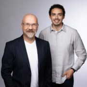 Two men in front of grey background.
