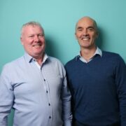 Two men in front of green background.