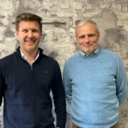 Two men in front of a stone wall.