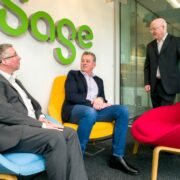 Two men sitting talking to one man standing.