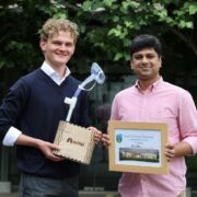 Two men holding prizes and a certificate.