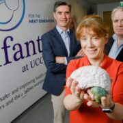 Woman in red holding a model of a brain beside two men.