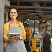 Woman in apron at door of a restaurant.