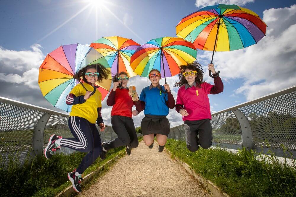 Four students jump in air with colourful umbrellas.