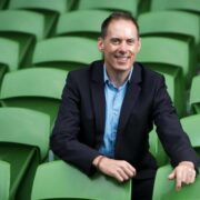 Man in navy jacket sitting in stadium.