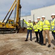 five people in hi vis jackets surveying a construction site beside a digger.