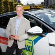 Man in cream jacket in front of a taxi.