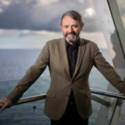 Man standing in building with sea in background.