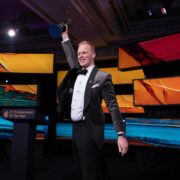 Man in tuxedo holding award aloft.