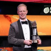 Man in tuxedo holding award.