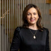 Dark-haired woman in black dress, gold pendant.