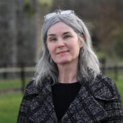 Woman in checkered coat standing in a field.