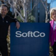 Man and woman in pink jacket either side of a sign that says SoftCo.