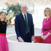 Two women and a man in a suit in a bright office environment.