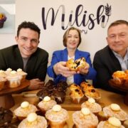 Two men and a woman with a table full of cakes.