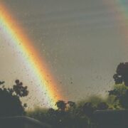 Clusters of rainbows appear amid a stormy sky as raindrops fall on a window.