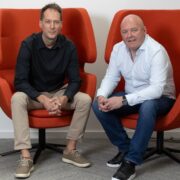 Two men sitting on orange chairs.