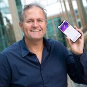 Smiling man in navy-blue shirt holding phone.