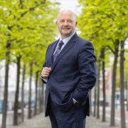 Man in dark suit standing amid trees in Dublin.