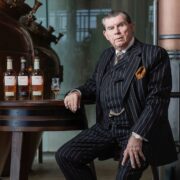 Man in pinstriped suit beside bottles of whiskey.