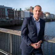 Man in suit leaning against bridge over Liffey in Dublin.