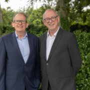 Two smiling men in business suits and glasses.