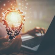 Businessperson working on laptop holding a light-bulb.