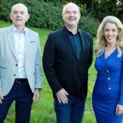 Two men beside woman in blue dress.