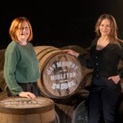 Two woman standing among whiskey barrels.