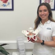 Woman in white t-shirt holding model of pelvic floor.