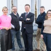 Three men and two women in front of a white building.