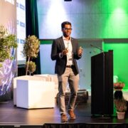 Man in sports jacket speaking on stage.